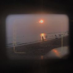 people are walking on the beach as the sun goes down in the sky over the water