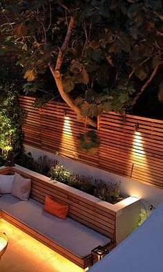 an outdoor seating area is lit up at night with lights on the benches and trees