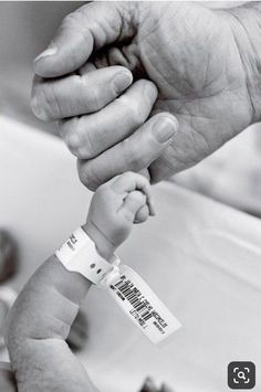 a black and white photo of a person holding a baby's hand