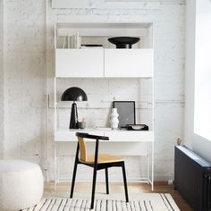 a white desk and chair in front of a brick wall with shelves on the side