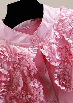 a pink dress with ruffles and buttons on the collared neckline is displayed