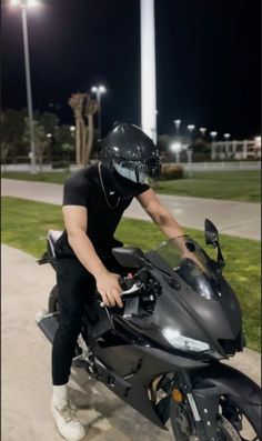 a man in black shirt and helmet sitting on a motor bike at night with street lights behind him