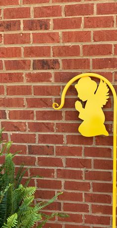 a yellow metal sign on the side of a brick wall next to a green plant