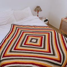 a crocheted blanket sitting on top of a bed next to a night stand