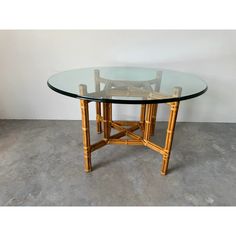 a round glass table with bamboo legs on concrete flooring in front of a white wall