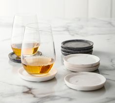 two glasses of wine on a marble table with white plates and black dishes in the background