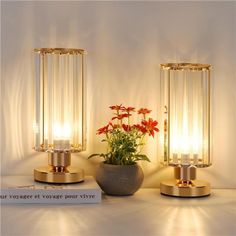 two glass vases with flowers in them on a table next to candles and a flower pot