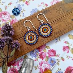 two pairs of earrings sitting on top of a table next to a ruler and flower