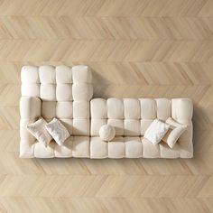 an aerial view of a white couch with pillows on the back and sides, against a wood floor