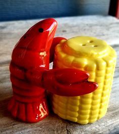 a red and yellow toy lobster next to a corn cob on a wooden table