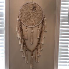 a white wall hanging with tassels and beads on the bottom, in front of a window