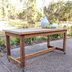 a wooden table sitting on top of a gravel ground next to trees and bushes in the background