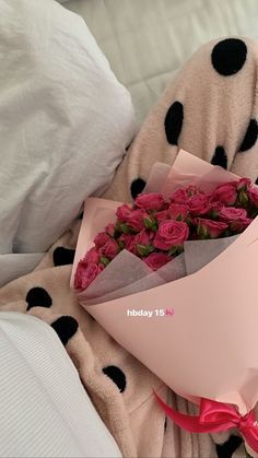 a bouquet of roses wrapped in pink and black polka dots sits on a white bed