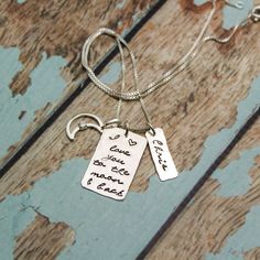 two silver tags with words on them are hanging from a wooden surface, one is attached to a chain