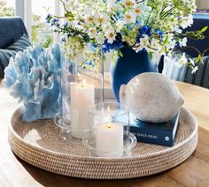 a table with flowers, candles and books on it in front of a blue vase