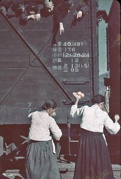 two women standing next to each other in front of a train car with people hanging from it