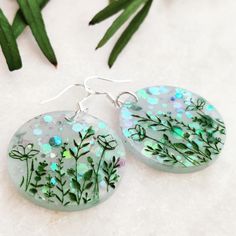 These lazy meadow flower earrings are made with a hit of white & green mica powder and chunky sparkly glitter. They are eye catching and light weight, and have been finished with a delicate green hand painted etched design. All items come ready for gifting carefully packaged in pretty tissue paper and a lovely beach themed Jute bag and charm. A white logo'd gift box is available for additional cost. Please select from variations. Why not browse our shop and take a look at our other listings. www.etsy.com/uk/shop/CraftyCurlewStudio Delivery - We aim to post all orders the next working day.  Free standard shipping in UK for items are sent via Royal Mail 2nd class. There is an option to upgrade to 1st class at checkout. Thanks for looking😊 Floral Meadow, Hand Painted Earrings, Beach Earrings, Summer Painting, Painted Earrings, Jute Bag, Meadow Flowers, Green Hand, Resin Painting