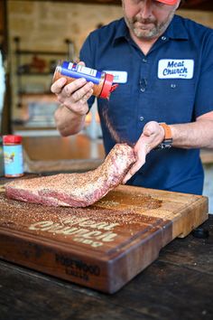 a man in blue shirt and red hat cutting up meat on wooden table with knife