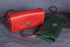 two leather purses sitting next to each other on a gray cloth covered tablecloth