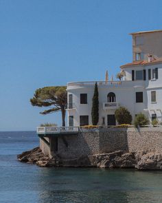 a large white house sitting on top of a cliff next to the ocean and trees