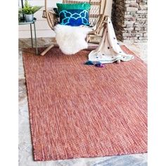 an outdoor area with a chair, rug and pillows on the ground next to a fire place