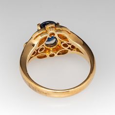 This gorgeous sapphire ring is centered with one (1) oval mixed cut natural sapphire set into a four-prong setting. The sapphire is bordered with fourteen (14), prong/bead set, round brilliant cut diamonds. The ring measures 11.3mm at the top, rises 6.2mm above the finger, tapering to 2.6mm wide and 1.0mm thick at the base of the shank. The ring is currently a size 6.25. Formal Fine Jewelry Sapphire Ring Oval Cabochon, Oval Cabochon Sapphire Ring For Formal Events, Formal Sapphire Ring With Bezel Setting And Oval Cabochon, Classic Oval Cabochon Sapphire Ring With Bezel Setting, Classic Sapphire Ring With Oval Cabochon Bezel Setting, Yellow Gold Sapphire Ring With Diamond Oval Cabochon, Yellow Gold Sapphire Diamond Ring With Oval Cabochon, Luxury Multi-stone Oval Sapphire Ring, Oval Cabochon Sapphire Ring In Yellow Gold With Diamond