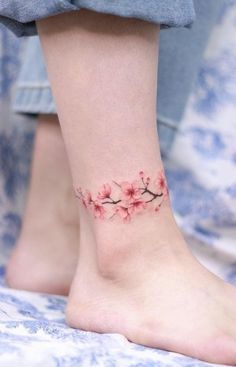 a woman's foot with a small tattoo on the ankle and pink flowers in bloom