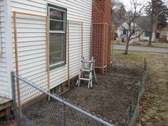 two chairs are sitting in the dirt near a house with a chain link fence around it