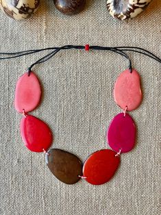 Handmade in Ecuador Necklace Length: Adjustable Length 14 -31 Inches Due to this item being handmade and the nature of the Tagua Nut the size and the color may vary from piece to piece Adjustable Red Nature-inspired Jewelry, Handmade Red Nature-inspired Necklace, Adjustable Multicolor Nature-inspired Jewelry, Multicolor Jewelry With Adjustable Cord, Red Bohemian Jewelry With Adjustable Cord, Pink Bohemian Resin Jewelry, Bohemian Red Jewelry With Adjustable Cord, Bohemian Pink Resin Jewelry, Handmade Pink Nature-inspired Jewelry