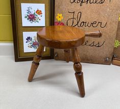 a small wooden stool sitting in front of a cork board with flowers on it next to a sign