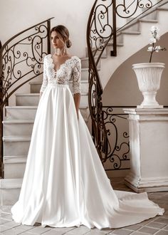 a woman standing in front of a staircase wearing a wedding dress with long sleeves and a low back