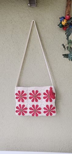 a white purse hanging on the wall next to a flower potted plant with red flowers