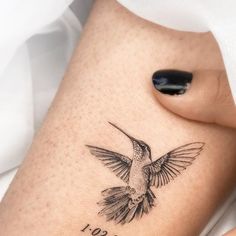 a small hummingbird tattoo on the side of a woman's leg, with her name written in cursive writing