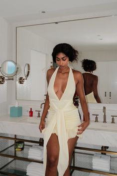 a woman standing in front of a bathroom mirror wearing a white dress and high heels