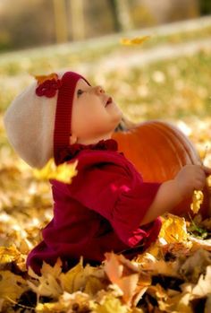 a small child in a red shirt and white hat is laying on the ground with leaves