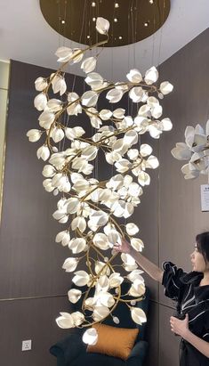 a woman standing in front of a chandelier with white flowers hanging from it