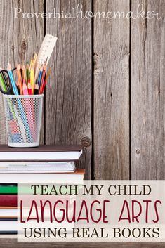 a stack of books sitting on top of a wooden table next to a cup filled with pencils