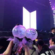 two people holding up balloons in front of a crowd at a convention or event with purple lighting