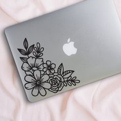 an apple laptop with black flowers on the back and white sheets in the bed behind it