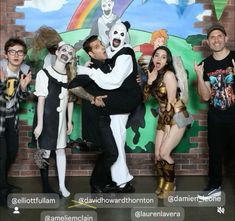 a group of people standing next to each other in front of a brick wall wearing costumes