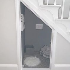 an open door leading to a small dog bed under the stairs in a white house