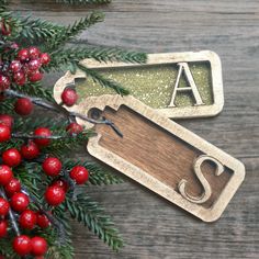 two wooden tags sitting on top of a table next to christmas tree branches and berries