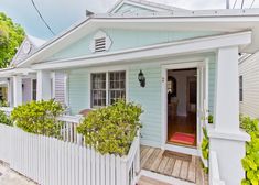 a blue house with white picket fence and green plants on the front porch, next to a wooden deck