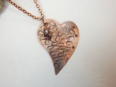 A totally unique stamped heart metal pendant. This metal heart is covered with random stamped hearts and adorned with tiny metal balls. To top it off, a metal or crystal bead is added to the top off the pendant. There are two color options - aluminum or copper. It is 24 inches long on lightweight chain. Bronze Heart Necklaces For Valentine's Day, Bronze Heart-shaped Necklace For Valentine's Day, Metal Heart Necklace With Open Heart Shape, Metal Heart Necklace With Heart Beads, Metal Heart Necklace With Open Heart And Heart Beads, Metal Open Heart Necklace With Heart Beads, Heart-shaped Silver Copper Jewelry, Silver Heart-shaped Copper Jewelry, Nickel Free Metal Heart Necklace