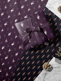 two presents wrapped in purple and gold wrapping paper with bows on them, sitting next to each other