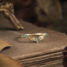 a gold ring with two green stones on top of it next to a stack of books