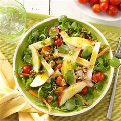 a salad with apples, lettuce and tomatoes in a bowl next to a glass of water