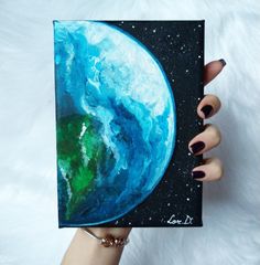 a woman's hand holding up a small painting with the earth painted on it