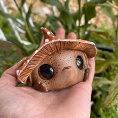 a hand holding a small wooden toy in front of some plants