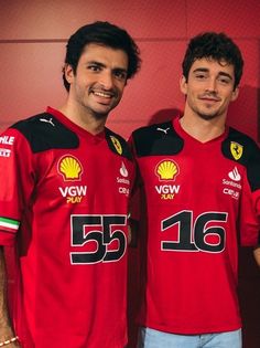 two men standing next to each other in front of a red wall